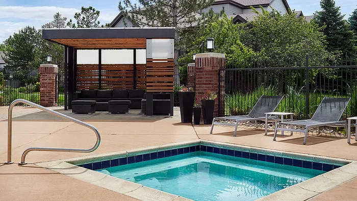 Chic outdoor lounge with modern seating, stylish cabana, and inviting hot tub in a lush garden setting.