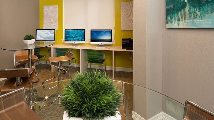Modern co-working space with sleek glass tables, vibrant yellow walls, and multiple computers for productivity.