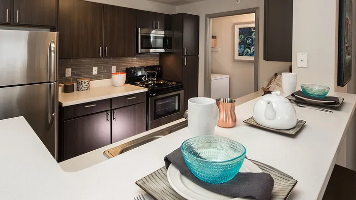 Modern kitchen with stainless steel appliances, elegant dark cabinetry, and chic countertop decor, featuring a vibrant blue bowl and stylish teapot.