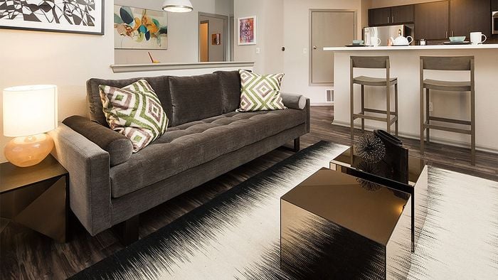 Modern living room with sleek grey sofa, chic geometric cushions, and a stylish kitchen bar with stools, exuding contemporary elegance.
