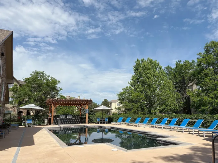 Inviting outdoor pool area surrounded by lush greenery and chic blue loungers under a clear blue sky.