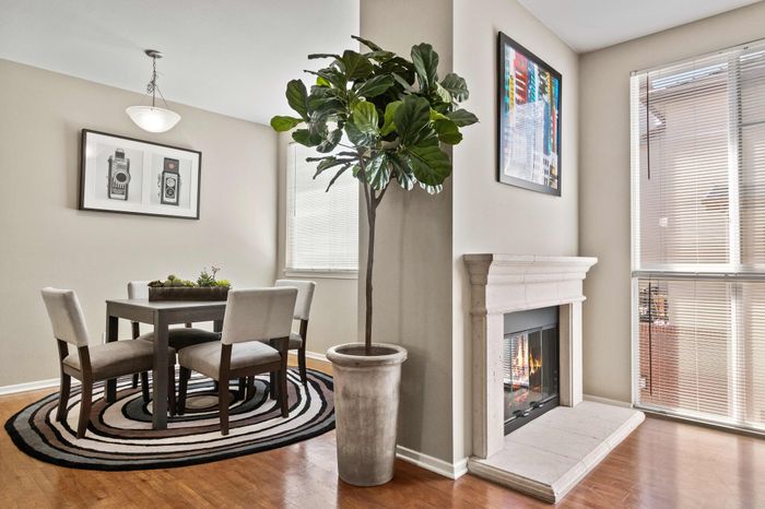Modern apartment interior with a cozy dining area featuring a chic circular rug, elegant fireplace, and large windows for natural light.