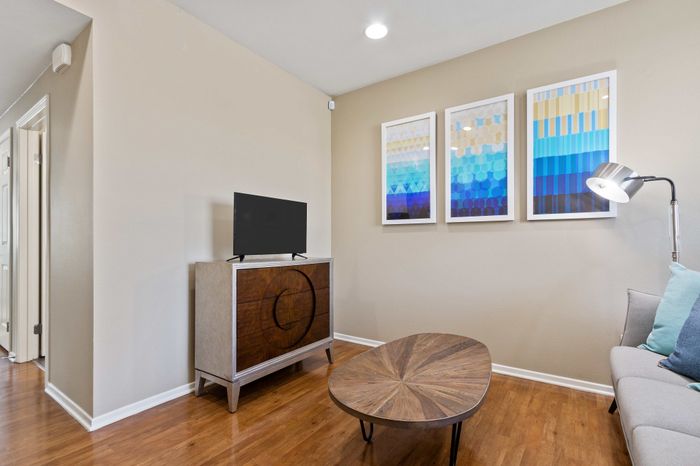 Elegant living area with modern decor, featuring a sleek TV stand, abstract blue artwork, and cozy seating on stylish wooden flooring.