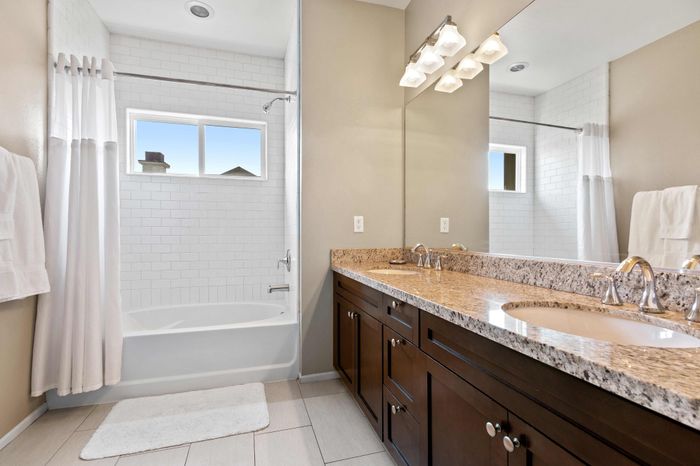 Bright and modern bathroom featuring dual sinks, elegant granite countertop, and sleek white tiles.