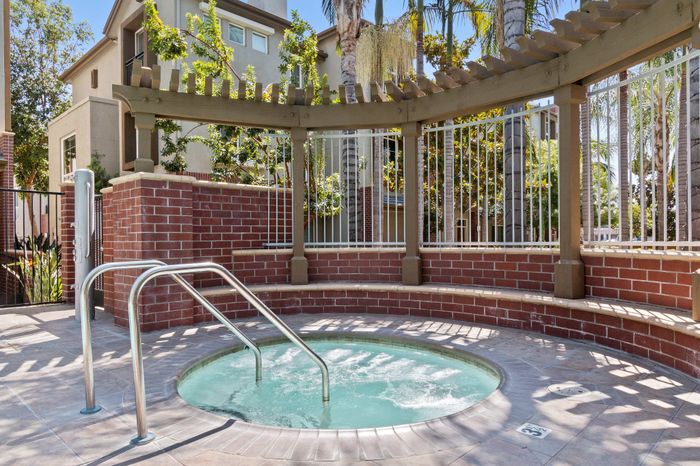 Inviting outdoor hot tub surrounded by lush greenery, brick accents, and a wooden pergola, perfect for relaxation.