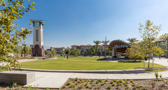 Charming park view showcasing a clock tower, lush green lawn, and modern residential buildings under a clear blue sky.