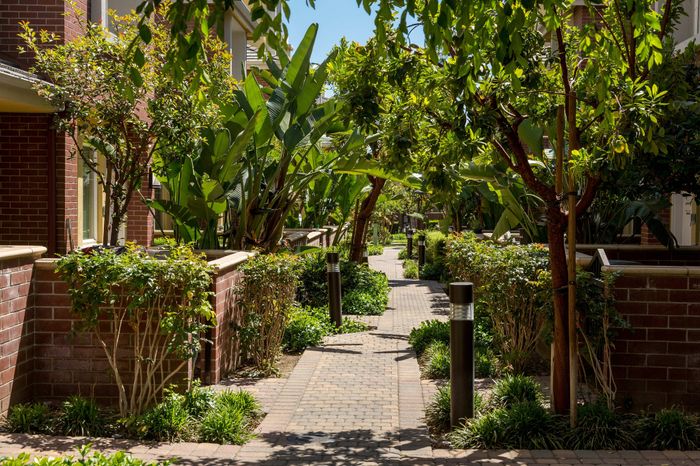 Beautiful apartment walkway lined with lush greenery and red brick walls, creating a serene and inviting environment.