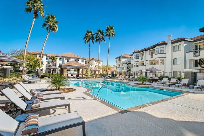 Luxurious apartment complex showcasing a pristine pool surrounded by elegant lounge chairs and vibrant palm trees under a clear blue sky.