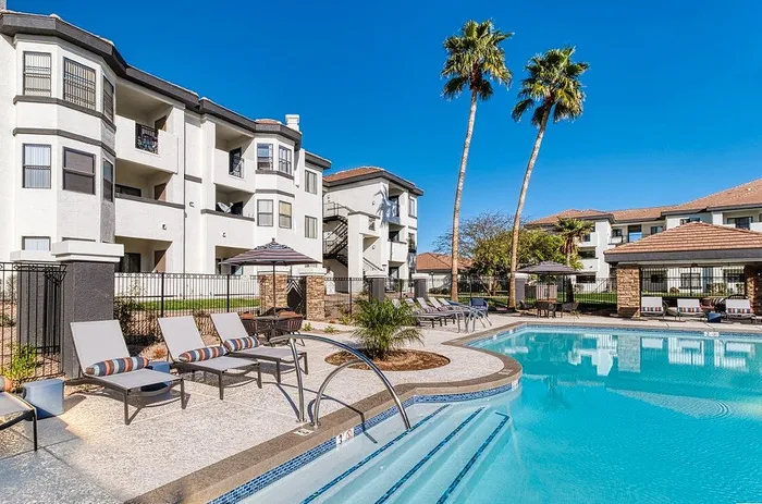 Luxurious apartment complex showcasing a sparkling pool, stylish lounge chairs, and towering palm trees on a sunny day.