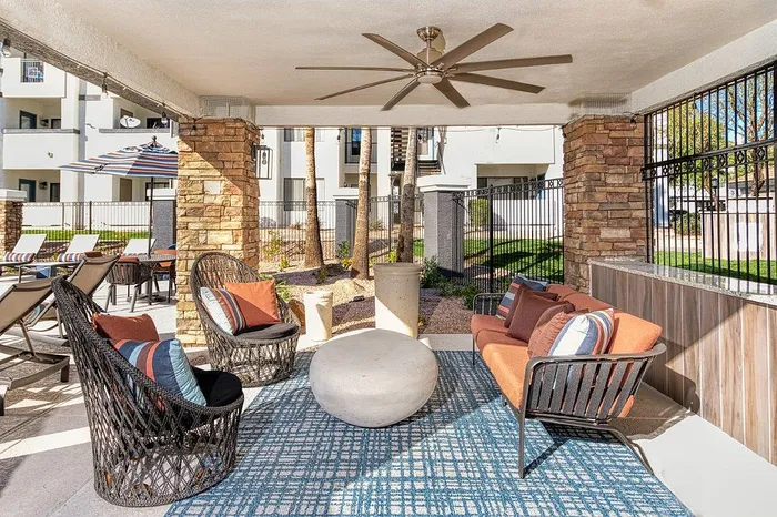 Chic outdoor lounge area with stylish wicker chairs, vibrant orange cushions, and a modern ceiling fan, perfect for relaxation.
