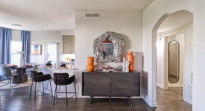 Modern apartment interior with stylish decor, featuring a cozy dining area next to a sleek breakfast bar with elegant stools, complemented by contemporary accessories and a unique wall mirror.