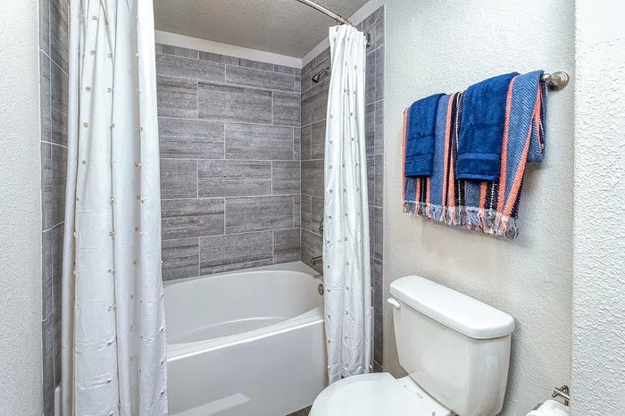 Modern bathroom with elegant gray tile walls, a sleek white bathtub, and vibrant blue towels adding a pop of color.