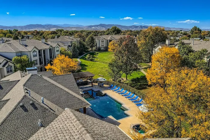 Scenic aerial view of a vibrant residential community featuring beautifully landscaped gardens, a sparkling swimming pool, and picturesque mountain views in the background.