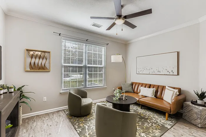 Chic living room with modern leather sofa, elegant armchairs, and botanical d&eacute;cor, inviting natural light through expansive windows.