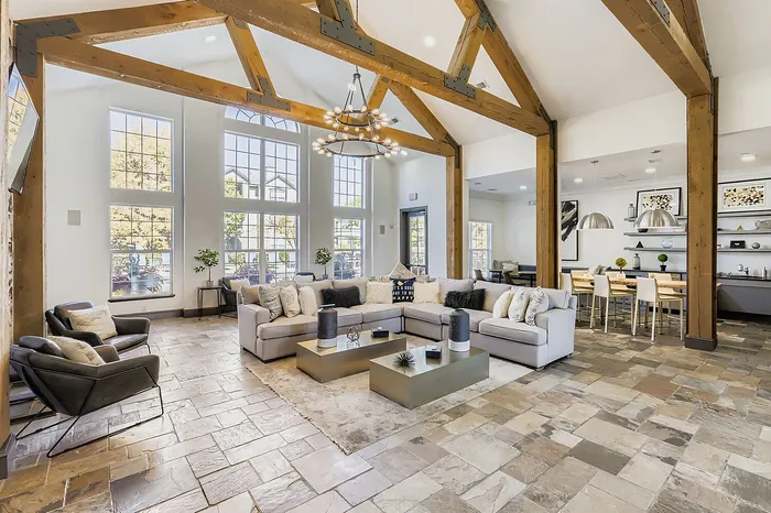 Stunning open-concept living area featuring high vaulted ceilings with exposed wooden beams, large windows offering abundant natural light, and a chic, cozy seating arrangement. Includes a modern dining space with sleek lighting and stylish decor, perfect for luxury living.