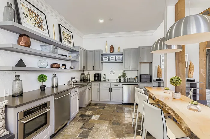 Chic modern kitchen featuring sleek gray cabinets, open shelving with stylish decor, and a unique live-edge wood dining table with contemporary lighting.