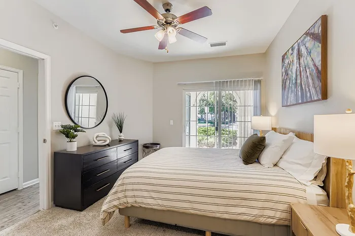 Inviting bedroom with sleek modern decor, featuring a plush bed, elegant ceiling fan, and serene view through large windows.