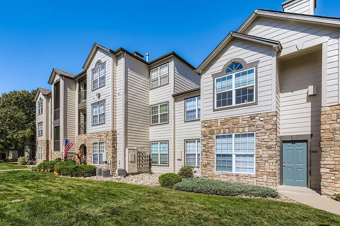 Charming apartment building with beautiful stone accents and well-manicured lawn, featuring modern multi-level units with large windows.