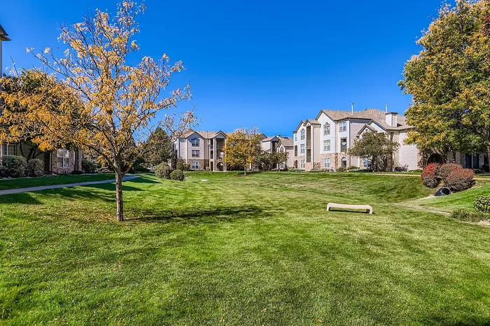 Charming apartment buildings surrounded by beautifully manicured lawns and vibrant autumn trees under a clear blue sky.