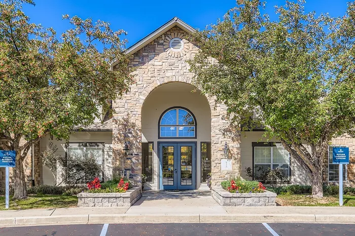 Charming stone facade entrance with arched windows, surrounded by lush greenery and vibrant flower beds, inviting and picturesque.