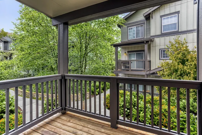 Charming apartment balcony with wooden railing, lush greenery, and scenic views of neighboring buildings.