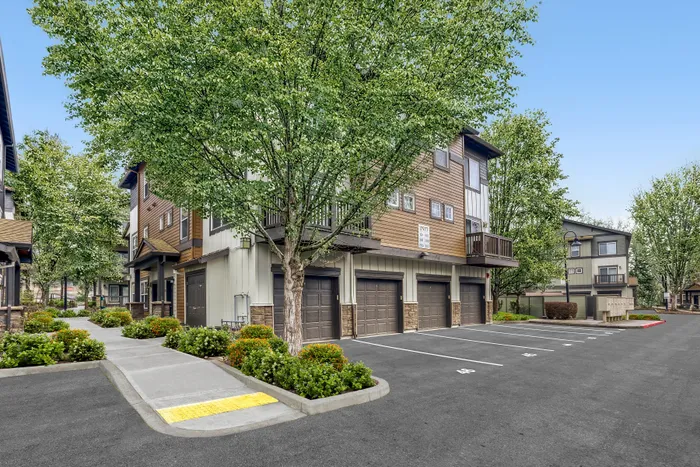 Charming modern townhouse exterior with lush landscaping, multiple garages, and scenic surroundings.