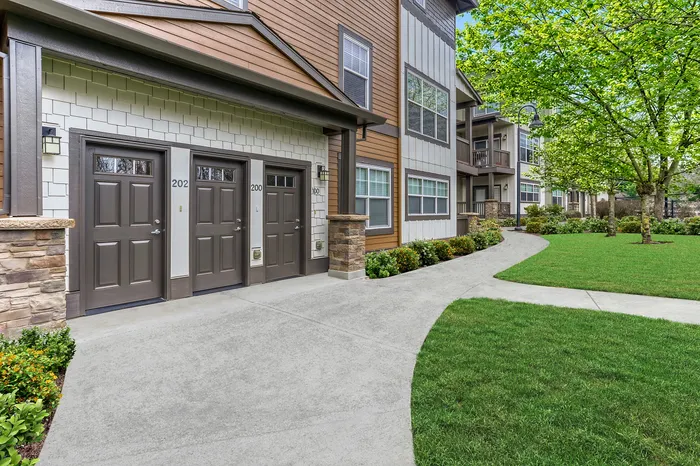 Charming apartment entrance with modern brown doors, surrounded by lush greenery and a well-maintained pathway.