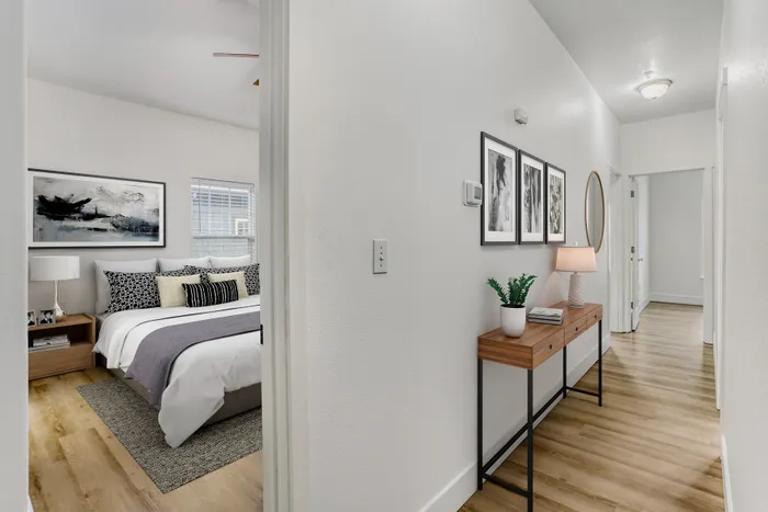 Inviting apartment hallway with elegant wood flooring leading to a cozy bedroom featuring modern decor and natural light.
