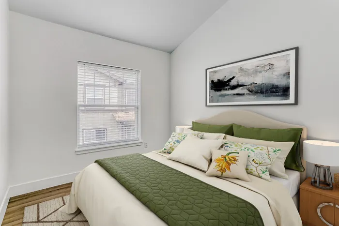 Inviting bedroom with a stylish bed adorned with green accents and floral pillows, complemented by elegant artwork and a large window providing natural light.