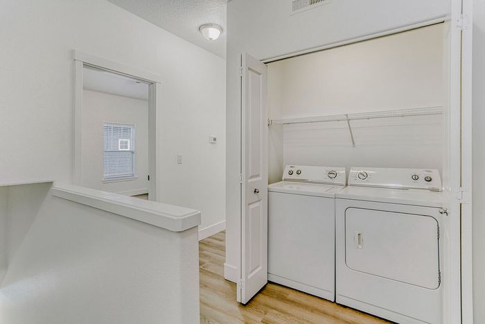 Bright and modern hallway featuring an in-unit laundry area with washer and dryer, accented by sleek wooden flooring.
