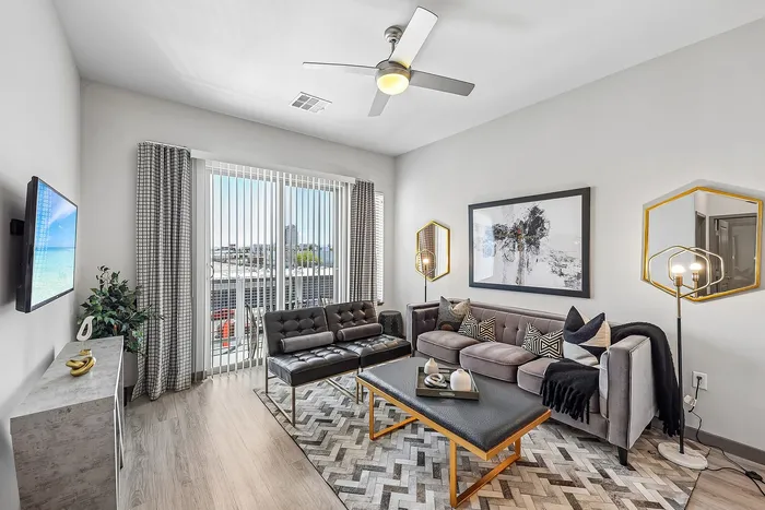 Modern living room with a sleek sofa set, geometric accents, and a large window offering abundant natural light.