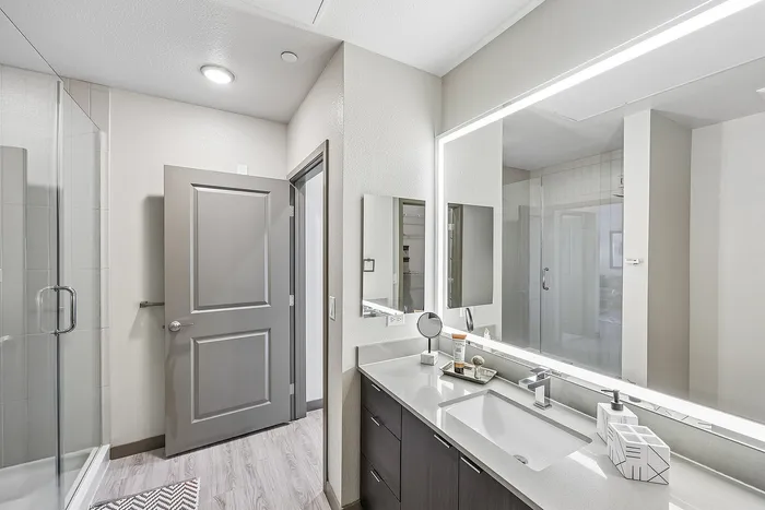 Modern bathroom showcasing a sleek vanity, bright mirrored lighting, and a spacious glass shower enclosure.