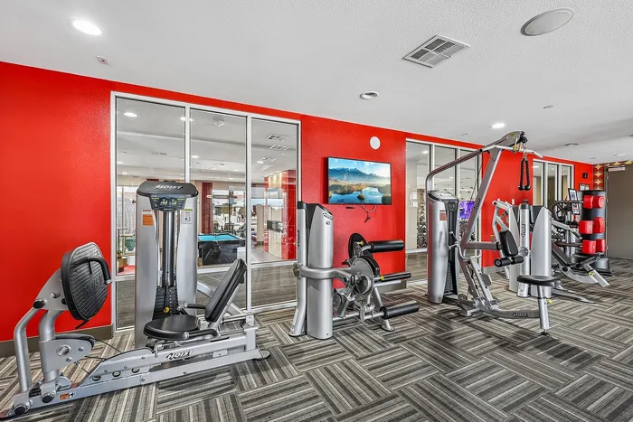 Contemporary fitness center featuring state-of-the-art exercise equipment against a vibrant red accent wall, perfect for a modern lifestyle.