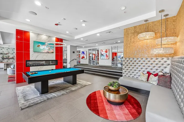 Modern apartment lounge with a sleek billiards table, vibrant red accents, plush seating, and elegant lighting.