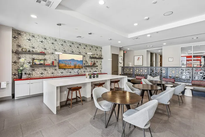 Modern communal space featuring elegant dining tables, stylish chairs, and a vibrant decorative wall with a large TV; ideal for social gatherings and relaxation.