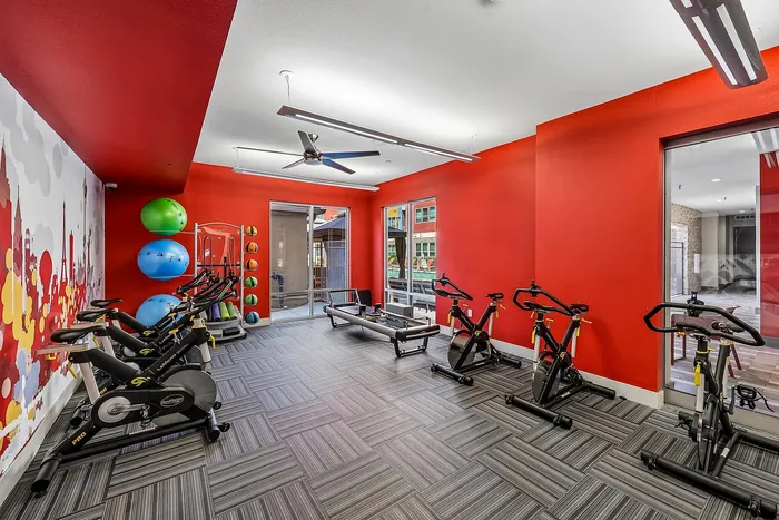 Modern fitness room featuring vibrant red walls, exercise bikes, colorful stability balls, and sleek flooring.