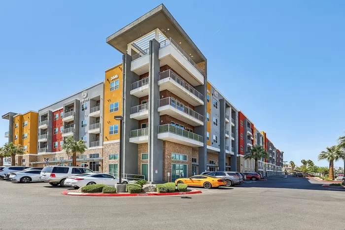 Vibrant modern apartment building with colorful balconies, lush palm trees, and ample parking under a clear blue sky.