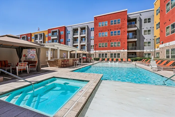 Vibrant apartment complex with inviting pool and spa, surrounded by colorful lounge chairs and modern architecture.