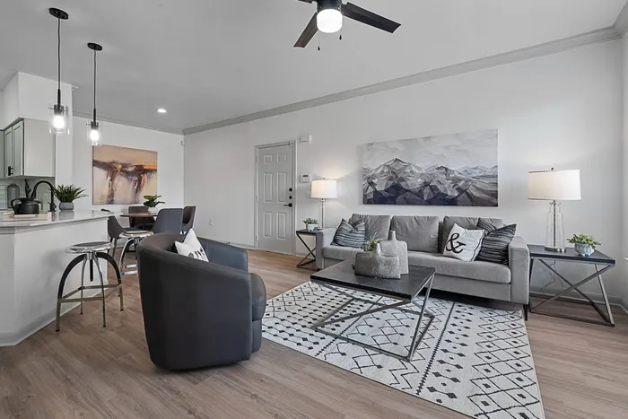 Model living room with modern furnishings, ceiling fan and hardwood style floors