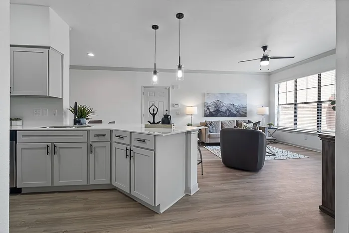 Model kitchen with breakfast bar, white cabinets, wood style flooring and living room in the background