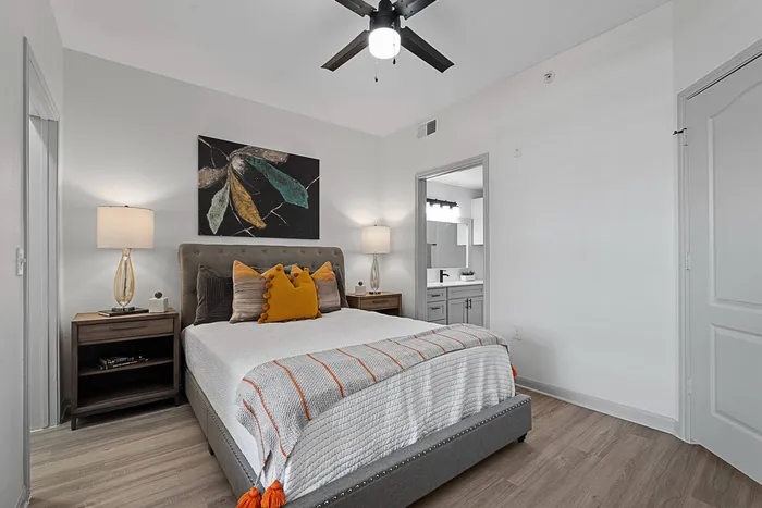 Model bedroom with large bed, ceiling fan, wood style floors and en suite bathroom
