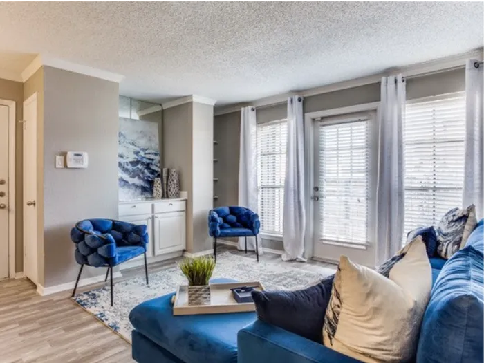 Vinyl floor living space with rug, blue couch, coffee table, ceiling fan, large windows,