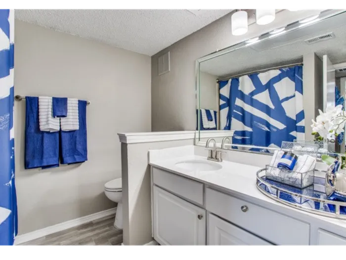 Bathroom with white counters, large mirror, vanity lighting, white cabinetry, shower, and toilet
