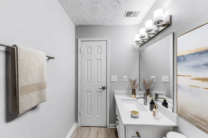 Bathroom with quartz counters, large mirror, vanity lighting, and white cabinetry