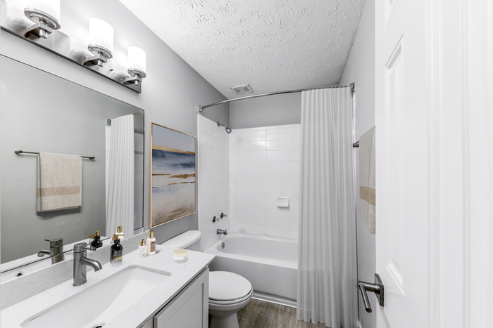 Bathroom with quartz counters, large mirror, vanity lighting, and white cabinetry
