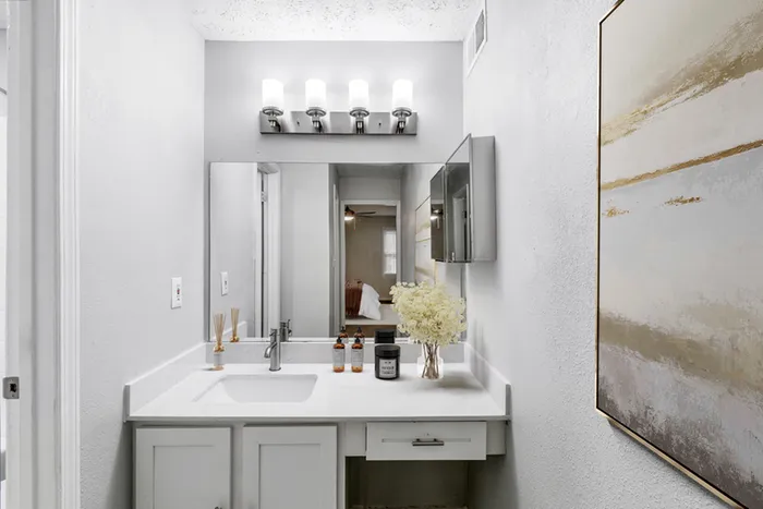 Bathroom with quartz counters, large mirror, vanity lighting, and white cabinetry