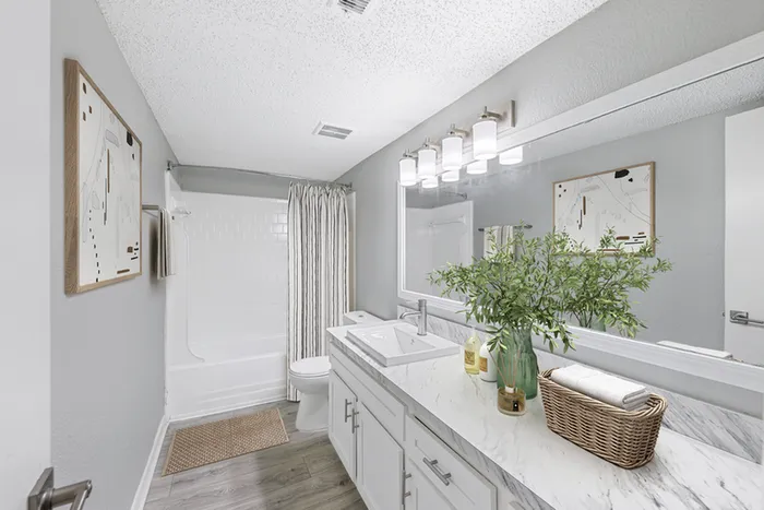 Bathroom with quartz counters, large mirror, vanity lighting, and white cabinetry