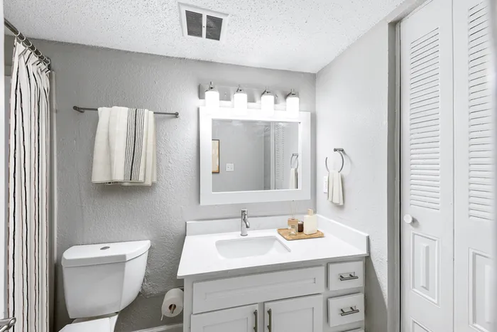 Bathroom with quartz counters, large mirror, vanity lighting, and white cabinetry