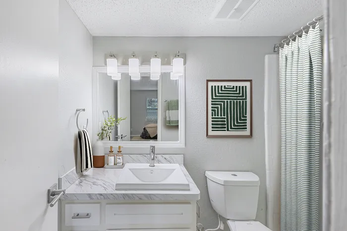 Bathroom with quartz counters, large mirror, vanity lighting, and white cabinetry