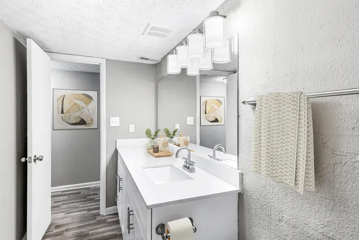 Bathroom with quartz counters, large mirror, vanity lighting, and white cabinetry